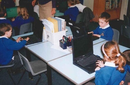 Dell Laptops 2002. Pupils in blue uniform working on laptops in classroom.