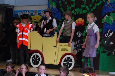Yr 6 production, Summer 2007. Pupils on stage in costume with yellow car.