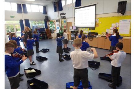 27 KS2 Violin Lessons. Pupil in school hall playing violins.